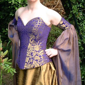 Brocade corset in gold and purple, fully boned and laced. The fabric is based on Arts and Crafts styles. Gauntlet style seperate sleeves with flowing chiffon mediaeval drapes. Matching gold silk skirt with small train.